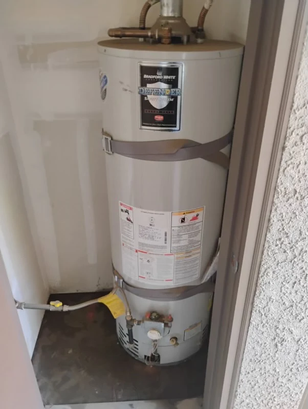 Water heater unit in a residential setting, labeled "Bradford White Defender," showcasing plumbing connections and safety information, relevant to plumbing services and installations.