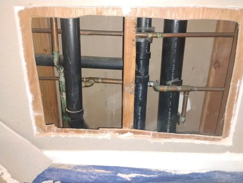Plumbing pipes and fittings visible through an opening in drywall, showcasing residential plumbing infrastructure for repairs and maintenance.